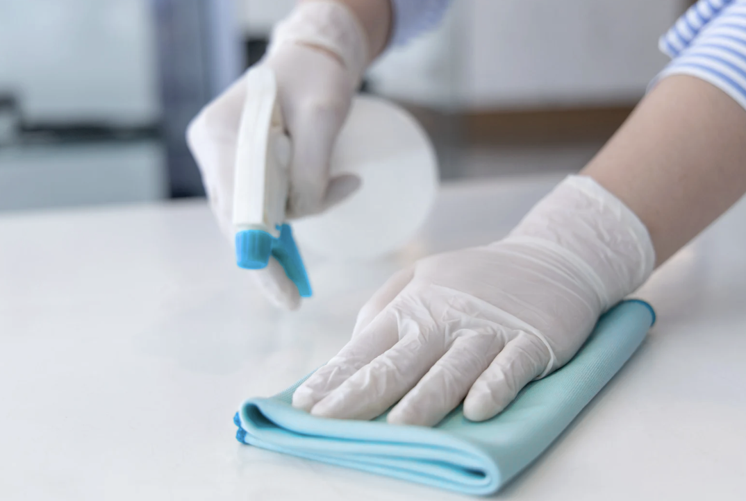 Behandschuhte Hände wischen mit Mikrofasertuch eine helle Oberfläche